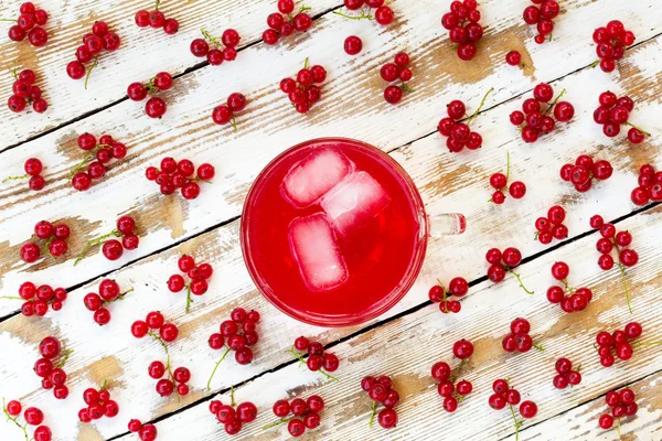 freshly squeezed red juice with ice cubes and bunches of red currants on a white wooden table with old paint. closeup flat lay