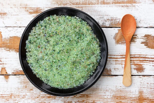 a tonic for the skin sea salt with pine concentrate in a black round dish and wooden spoon on wooden background with remnants of old white paint, close-up top view