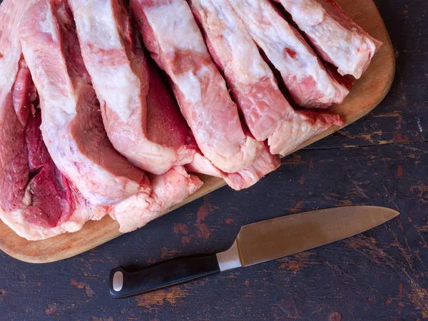 Ein großes Stück rohes Schweinefleisch in Stücke gehackt auf einem Schneidebrett auf einem alten rustikalen Tisch schwarz und Edelstahl-Küchenmesser, Nahaufnahme von oben — Stockfoto