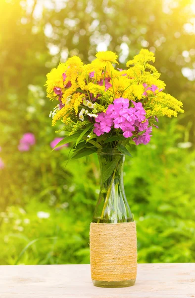 Un bouquet de fleurs de verge d'or, phlox et lis dans une bouteille en verre sur fond naturel dans les rayons dorés du soleil — Photo