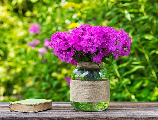 Bouquet de fleurs de phlox dans un vase en verre et un vieux livre sur la table sur fond nature, mise au point sélective — Photo