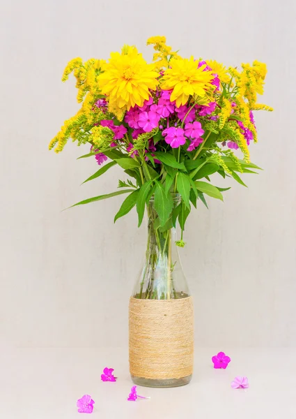 Un bouquet de fleurs de verge d'or, chrysanthèmes, phlox dans un vase en verre sur fond gris — Photo