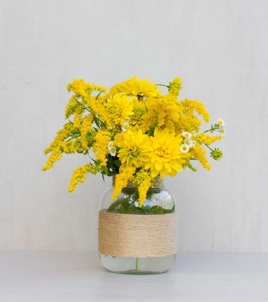 Um buquê de flores de goldenrod e crisântemos em um vaso de vidro caseiro closeup em fundo cinza closeup — Fotografia de Stock