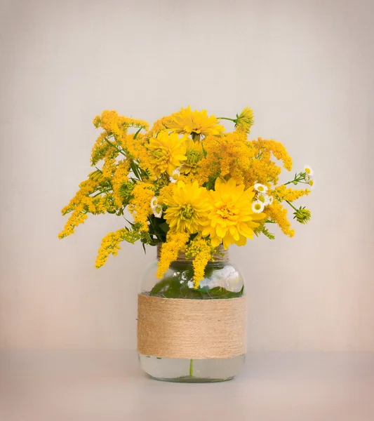 Um buquê de flores de goldenrod e crisântemos em um vaso de vidro caseiro closeup em fundo cinzento closeup. foto matizado — Fotografia de Stock