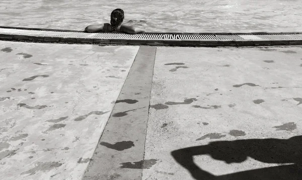 Chica en la piscina, un hombre sombra y rastros de pies mojados en el suelo. foto en blanco y negro — Foto de Stock