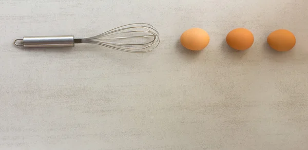 Frusta in acciaio e uova foderate in fila su fondo grigio. con spazio per testo — Foto Stock