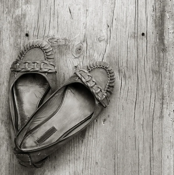 Old worn women's shoes made of genuine leather on old gray wooden board in the cracks, top view close-up. black and white photo — Stock Photo, Image