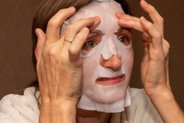 Genç bir kadın yüzüne beyaz nemlendirici bir maske takıyor.