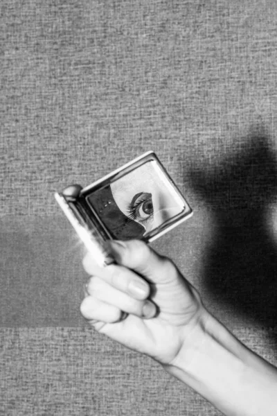 mirror in hand and reflection of the eye and moisturizing mask on the face of a young woman, black and white photo