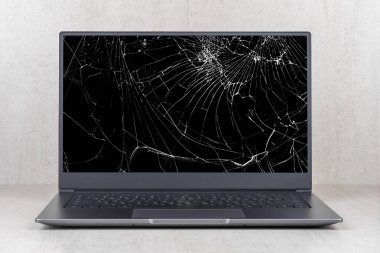 Gri arkaplandaki çatlaklar içinde kırık bir ekranı olan dizüstü bilgisayar ön görünümü kapat