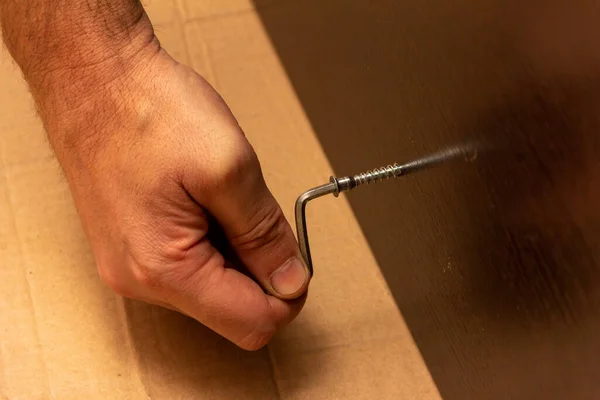 male hand tightens the screw with a hex wrench in dark brown laminated chipboard, furniture assembly