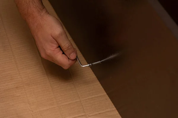 male hand tightening the screw with a hex wrench in a dark brown laminated chipboard, furniture Assembly
