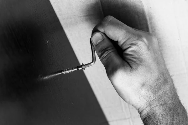 male hand tightening the screw with a hex wrench in a laminated chipboard, furniture Assembly, black and white photo