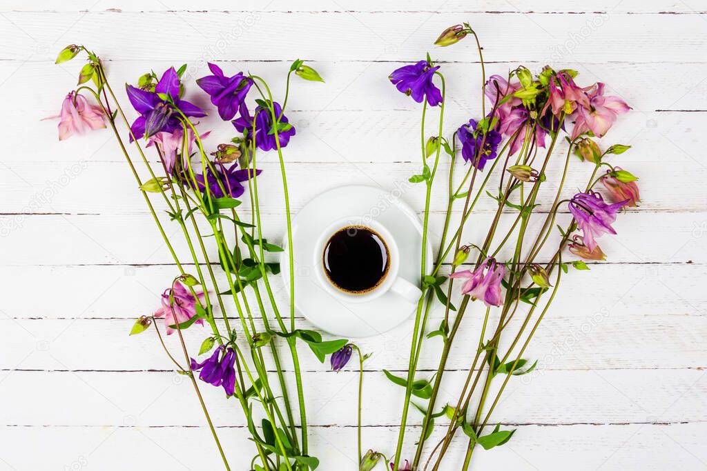 cup with coffee on a white wooden table with pink and blue aquilegia flowers top view