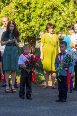 Adygea, Rusya - 1 Eylül 2020: Birinci sınıf çocukları okul bahçesinde öğrenim gününde çiçek buketleri ve aileleri ile
