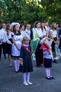 Adigea, Rusya - 1 Eylül 2020: Birinci sınıf öğrencisi bir kız buketli çiçekler ve lise öğrencileri bilgelik gününde resmi çizgide