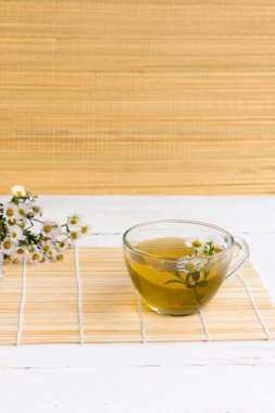 Bambu hasır bambu arka plan duvar kağıdı üzerinde taze papatya çiçekler çevrili eski Beyaz ahşap masa üzerinde bir fincan taze papatya çiçeği ile açık cam fincan papatya çayı