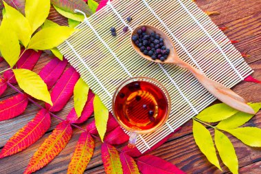 infüzyon alıç bir cam kase, Kuru Meyve ve bambu hasır parlak sarı ve Kızıl sonbahar yaprakları ile masada tahta kaşıkla