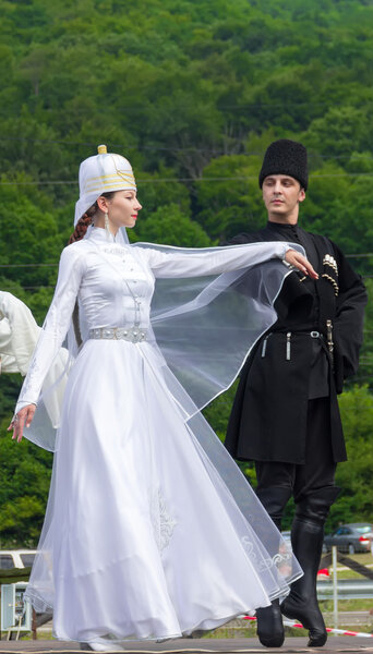 Young guy with a girl in Adyghe national costumes dancing traditional dance at an ethnofestival in the Foothills of Caucasus in Adygea