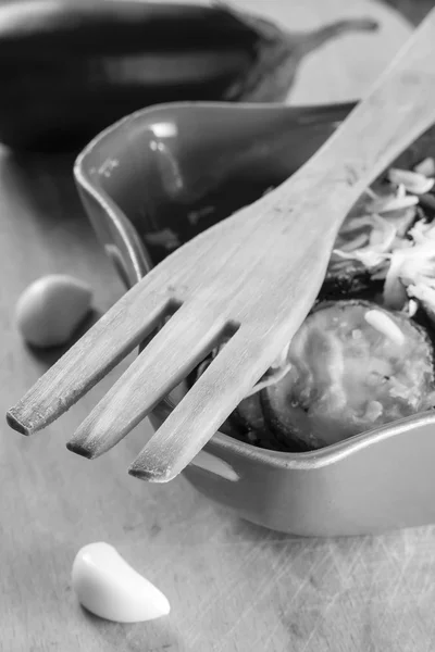 Tenedor de madera, berenjena frita con ajo en un tazón de cerámica y dientes crudos de ajo y berenjena en blanco y negro, enfoque selectivo — Foto de Stock