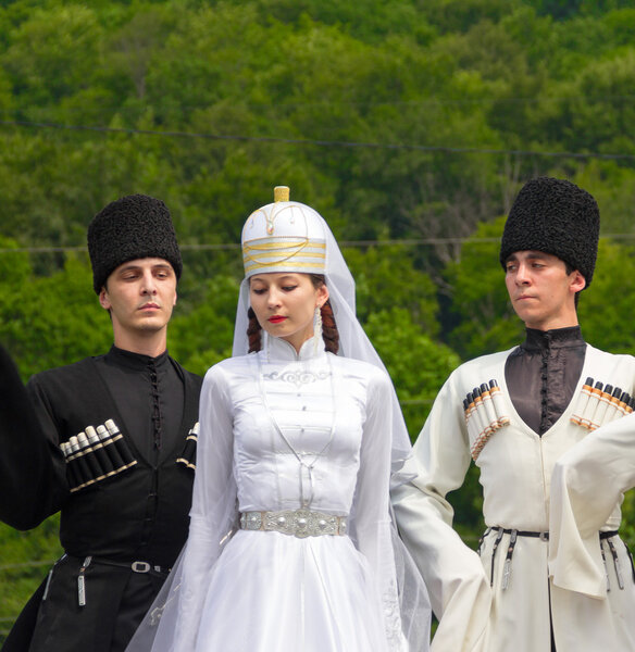 Молодые парни и танцовщицы в традиционных адыгейских платьях, танцуют на этнофестивале у подножия Западного Кавказа в Адыгее
