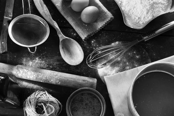 Eine Reihe alter Küchenutensilien aus der Nahsicht von oben. Küchentisch im rustikalen Stil. Produkte zum Backen von Mehl, Eiern, Salz. Schwarz-Weiß-Foto — Stockfoto