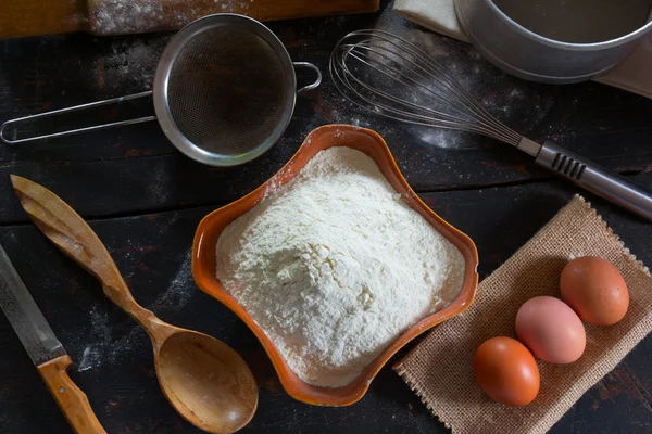 Geschirr und Lebensmittel am alten heimischen Schreibtisch. Weizenmehl in einer Keramikschale und Hühnereier für die Teigzubereitung. rustikaler Stil. Nahaufnahme von oben. — Stockfoto