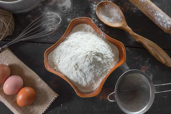 Mesa de cocina antigua con utensilios y productos para la prueba. Harina de trigo en un plato de cerámica y huevos de pollo para la preparación de la masa. Estilo rústico. Vista superior de cerca . — Foto de Stock