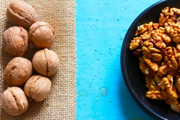 Parte de una placa de madera redonda con nueces sin cáscara y arpillera con las nueces marrones sobre un fondo azul. Espacio libre para texto. Copiar espacio — Foto de Stock