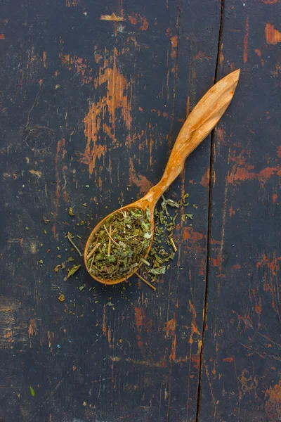 Herbes séchées dans une cuillère en bois sur le vieux fond noir fissuré. Ingrédient pour la cuisson de boissons saines. Le concept de phytothérapie rustique — Photo