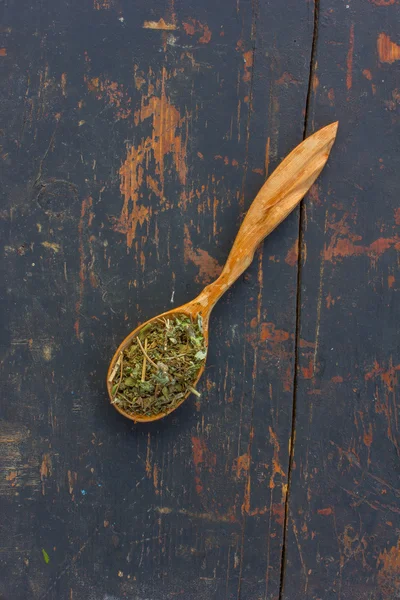 Hierbas secas en una cuchara de madera sobre el viejo fondo negro agrietado. Ingrediente para cocinar bebidas saludables. El concepto de terapia herbal rústica —  Fotos de Stock