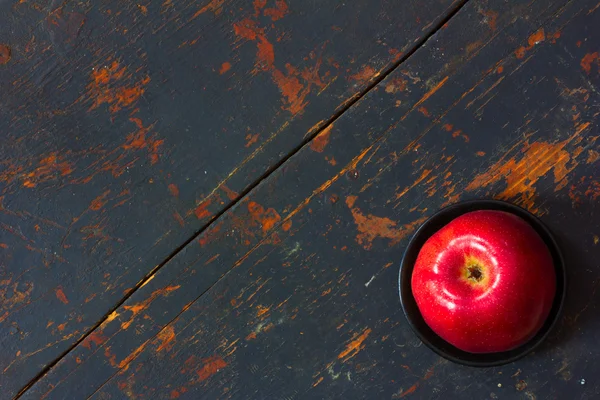 Pomme mûre rouge dans une soucoupe noire sur une vieille planche fissurée avec des taches dans le coin inférieur droit. Espace de copie. Espace libre pour le texte, Gros plan, vue du dessus — Photo
