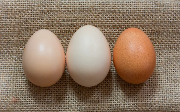 Three raw chicken eggs in shell laid out in a row on the gunny, Close-up, top view — Stock Photo, Image