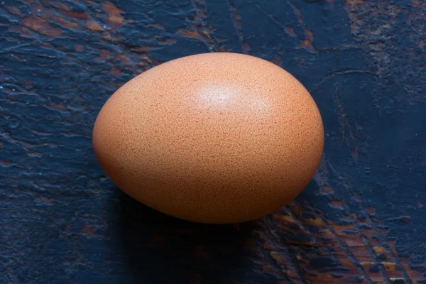 Brown raw chicken egg in shell on old blue wooden background. Close-up, top view — Stock Photo, Image