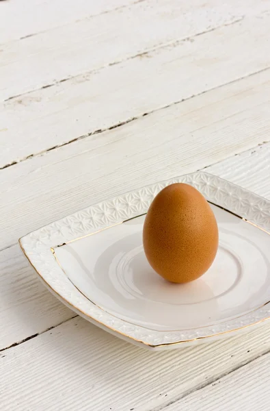 Brown chicken egg in the shell on a white ceramic saucer. Selective focus. Copy space. Free space for text — Stock Photo, Image