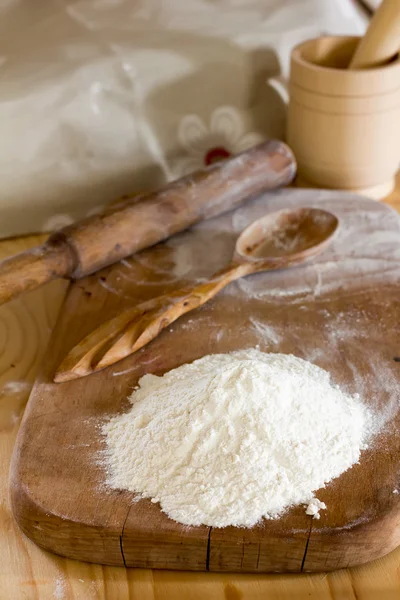 Segenggam tepung dan sendok kayu di papan potong dan rolling pin dengan mortir dan alu di atas meja. konsep tentang toko roti pedesaan, fokus selektif — Stok Foto