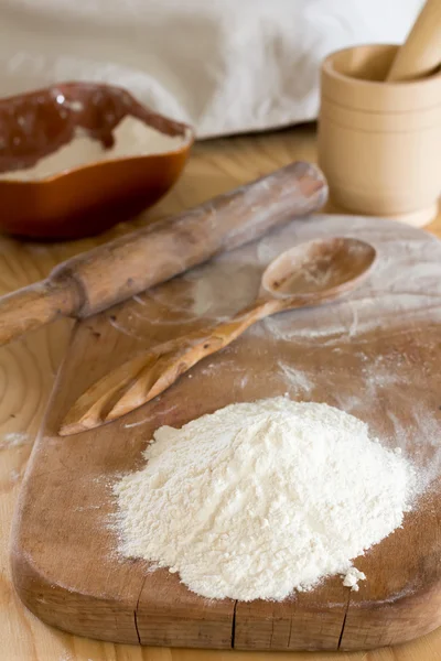 Eine Handvoll Mehl und ein Holzlöffel auf einem Schneidebrett und Nudelholz mit Mörser und Stößel auf dem Tisch. ländliches Bäckereikonzept, selektiver Fokus — Stockfoto