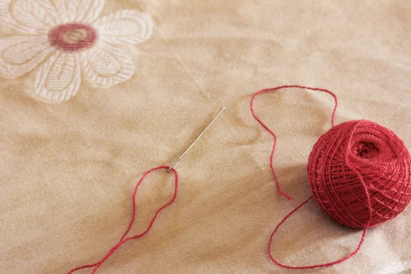 Le fil passé dans une aiguille et une boule de fils rouges contre le tissu de lin avec dessin — Photo