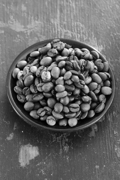 Roasted coffee beans in a round black saucer on old wooden background closeup. black and white photo