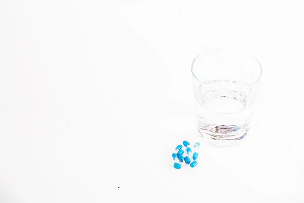 Стакан воды с лекарственными капсулами на белом фоне — стоковое фото