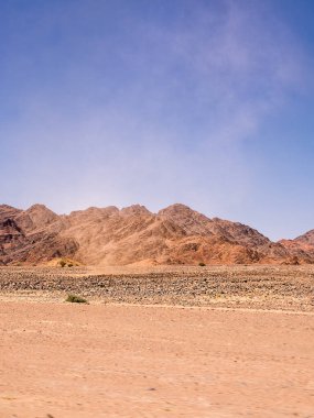 Uzak dağları olan kızıl kayalık çöl ayrıntıları ve rüzgarın savurduğu toz bulutu.
