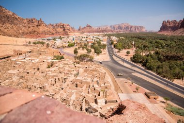 Al Ula, Suudi Arabistan - 24 Nisan 2025: El Ula Suudi Arabistan 'da tarihi çöl manzarasının arka planında dağlar ve palmiye ağaçları olan eski şehrin kalıntıları geçildi