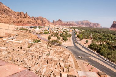 Al Ula, Suudi Arabistan - 24 Nisan 2025: El Ula Suudi Arabistan 'da tarihi çöl manzarasının arka planında dağlar ve palmiye ağaçları olan eski şehrin kalıntıları geçildi