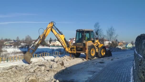 Moscú, Rusia - 2 de febrero de 2021: tractor limpia la nieve y el hielo de la carretera de la ciudad. Arado de nieve tractor rompe y elimina el hielo de una calle de la ciudad después de una nevada — Vídeos de Stock