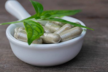 Andrographis, tahta arka planda beyaz bir kapsülde panikliyor..