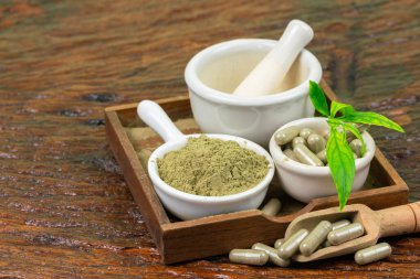 Andrographis tozunu beyaz bardaklarda ve Andrographis Paniculata bitkisel kapsüllerinde (Andrographis Paniculata) beyaz fincanda ve tahta kaşıkta, ahşap arka planda