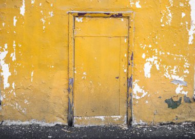 Çalışmayan kapısı ve eski kaldırımı olan eski sarı alçıdan bir duvar..