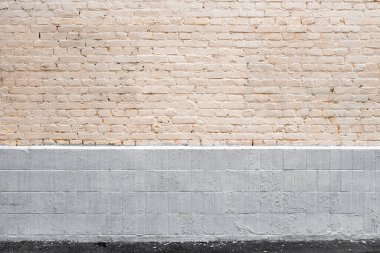 Eski soluk sarı tuğla duvar, döşeme ve boyanmış gri kaide ve gri asfalt kaldırım arka plan olarak.