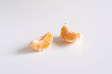 Beyaz arkaplanda soyulmuş mandalina dilimleri.