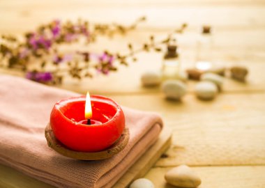Aroma terapi spa seti konsepti. Masaj yağı ve çakıl taşlarının bulanık görüntüsü olan pembe havlunun üzerinde mum, ahşap arka planda çiçekler. Lüks otel ya da profesyonel masaj için.